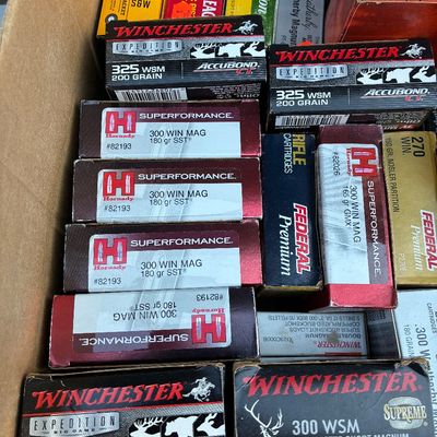 Sale Photo Thumbnail #56: Cardboard box filled with assorted boxed rifle ammunition, including brands like Winchester, Hornady Superperformance, Federal Premium, and Remington in various calibers.