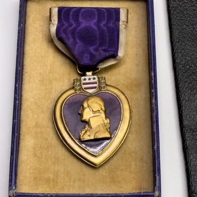 Sale Photo Thumbnail #42: U.S. Purple Heart military medal featuring a gold-tone profile of George Washington against purple enamel, complete with ribbon in its original blue presentation box.