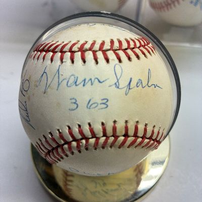Sale Photo Thumbnail #99: Autographed Warren Spahn baseball, featuring blue ink signature with '363' inscription, displayed in a clear acrylic cube with a gold-tone base.