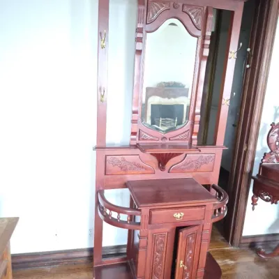 Sale Photo Thumbnail #7: Ornate Victorian-style carved wooden hall tree with a central mirror, brass coat hooks, integrated umbrella stands, and lower storage cabinet.