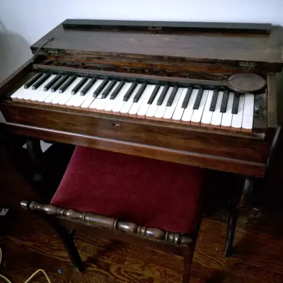 Sale Photo Thumbnail #47: Antique wooden melodeon pump organ with hinged top lid, paired with a matching wooden bench featuring a red upholstered seat.