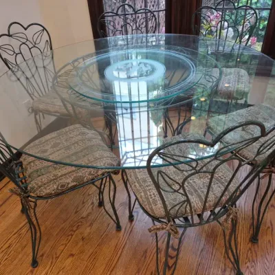 Sale Photo Thumbnail #24: Wrought iron dining set featuring a round glass-top table with a built-in lazy Susan and six matching chairs with leaf-motif backs and patterned seat cushions.