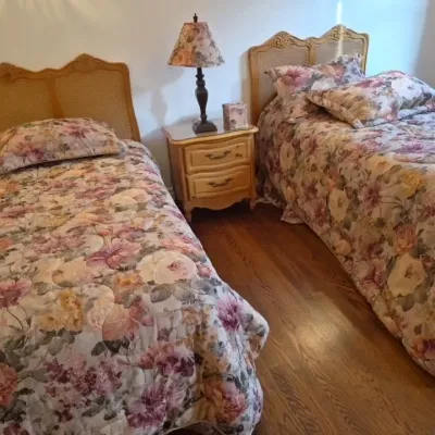 Sale Photo Thumbnail #39: Pair of French Provincial style twin beds with cane-back headboards, matching floral bedding, and a two-drawer nightstand.