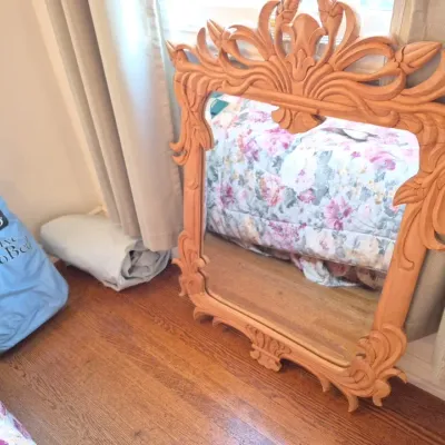 Sale Photo Thumbnail #45: Large ornate carved wood wall mirror leaning against a wall, accompanied by a blue AeroBed storage bag.