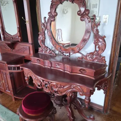 Sale Photo Thumbnail #6: Victorian-style ornate carved mahogany vanity table with attached oval mirror and matching red velvet cushioned stool.