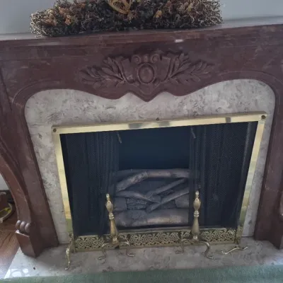 Sale Photo Thumbnail #33: Ornate French-style carved reddish-brown marble fireplace surround featuring central crest detail, paired with a brass screen, mesh curtains, and fire tools.