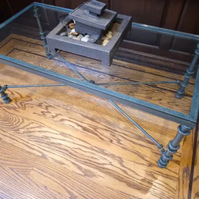Sale Photo Thumbnail #23: Rectangular glass-top coffee table featuring a dark textured metal frame with X-stretchers and ringed legs, topped with a stone-look tabletop fountain.