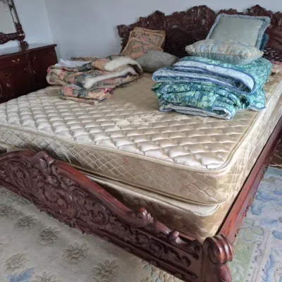 Sale Photo Thumbnail #35: Elaborately hand-carved dark wood bed frame with ornate floral scrolls, paired with a mattress and folded floral linens.