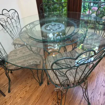 Sale Photo Thumbnail #60: Round glass-top dining table with a lazy Susan insert and four matching wrought iron chairs featuring heart-and-leaf motif backs.