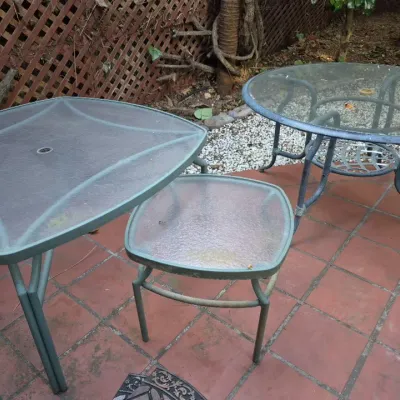 Sale Photo Thumbnail #12: Collection of outdoor patio tables, including a large glass-top dining table, a round glass-top table, and a small side table.