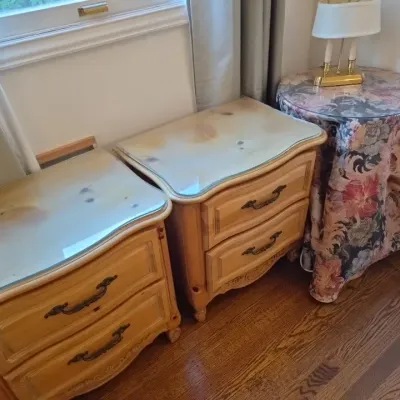 Sale Photo Thumbnail #41: Pair of French Provincial style light pine nightstands with glass tops and brass hardware, alongside a fabric-draped round accent table.