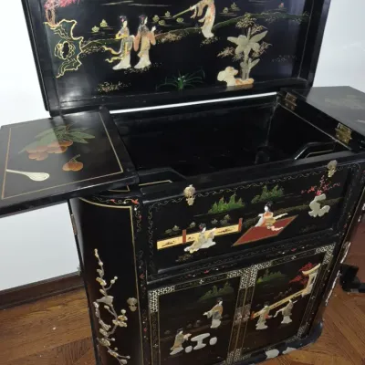 Sale Photo Thumbnail #4: Vintage Asian black lacquer dry bar cabinet with carved mother-of-pearl and stone figures, featuring a fold-out top and lower storage cabinet.