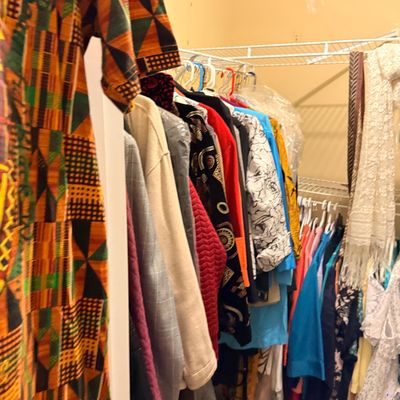 Walk-in closet filled with vintage women's clothing, including a Kente cloth print dress, embroidered jackets, scarves, and colorful...