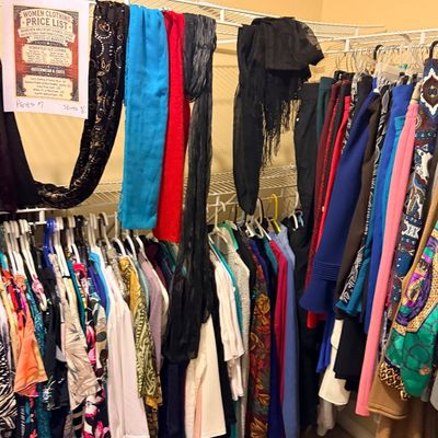 Walk-in closet filled with assorted women's clothing, including colorful dresses, blouses, skirts, and scarves draped over white...