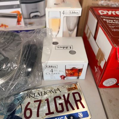 A collection of household goods featuring an Oklahoma license plate, boxed Libbey glassware sets, Pyrex cookware, and small kitchen...