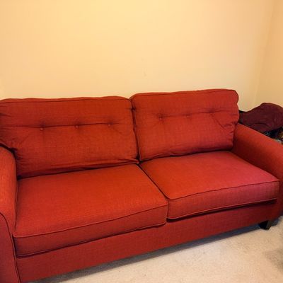 Contemporary red upholstered sofa featuring button-tufted back cushions, rolled arms, and dark wood feet.