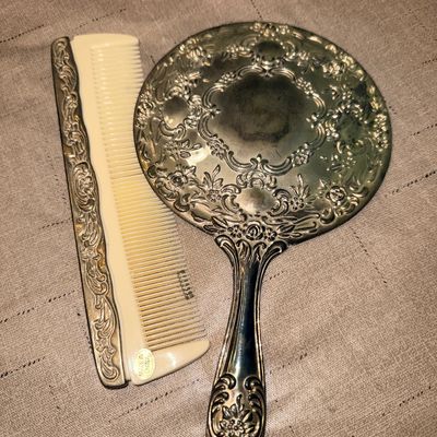 Vintage-style silver-plated vanity set featuring a heavily embossed hand mirror and matching spine comb with plastic teeth.