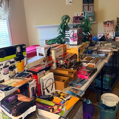 Assorted boxed small kitchen appliances, housewares, and personal care products arranged on folding tables.