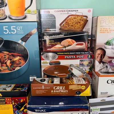 Collection of boxed kitchen appliances and cookware, including a Rival Crock-Pot, Gotham Steel pasta pot, Ninja blender, and Copper Chef...