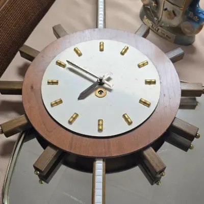 Sale Photo Thumbnail #40: Vintage mid-century starburst/ship wheel wall clock featuring a wooden ring frame, brass hour markers, and extended arms with white inlay accents.