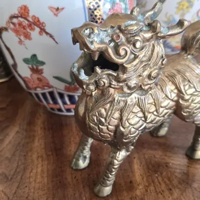 Sale Photo Thumbnail #51: Vintage brass Qilin (mythological dragon lion) figurine, sitting on a wooden tabletop in front of decorative Asian porcelain ginger jars.