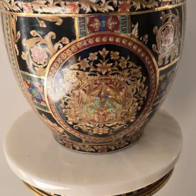 Sale Photo Thumbnail #47: Ornate Chinese black-ground fishbowl planter featuring gilt and polychrome floral medallions, resting on a gilt pedestal with a white marble top.