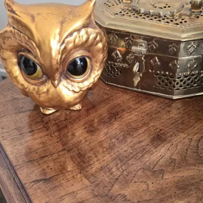 Sale Photo Thumbnail #52: Vintage gold-toned owl figurine with glass eyes displayed alongside an ornate pierced brass trinket box on a wooden tabletop.