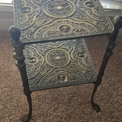Sale Photo Thumbnail #24: Victorian style ornate cast metal two-tier plant stand or side table featuring elaborate relief scrollwork, cherub motifs, and claw feet.
