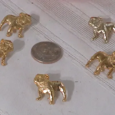 Set of five miniature gold-tone bulldog figurines arranged around a coin for scale.