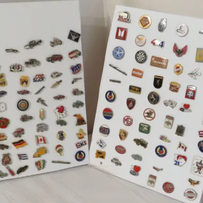Large collection of vintage enamel and metal lapel pins displayed on two white boards, featuring automotive, pop culture, and novelty...
