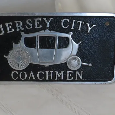 Vintage Jersey City Coachmen cast metal license plate topper featuring a raised carriage graphic and lettering on a textured black...