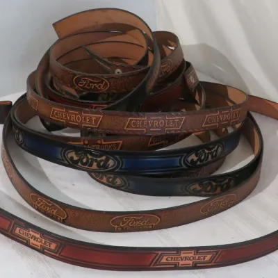 Collection of coiled tooling-embossed leather belts featuring Ford and Chevrolet logos.