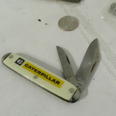 Vintage Caterpillar promotional two-blade pocket knife with off-white casing, displayed next to a U.S. quarter for scale.