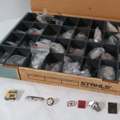 Stahls' cardboard storage tray filled with individually bagged lapel pins, displayed alongside a loose selection of novel...