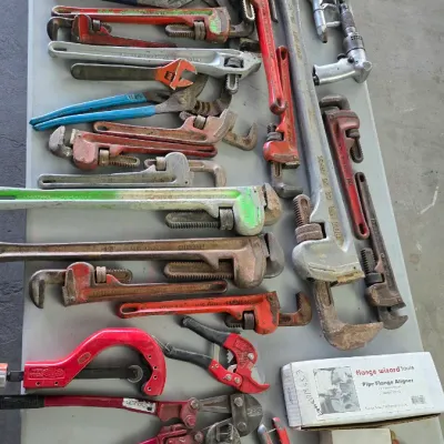 Sale Photo Thumbnail #78: Large assortment of vintage and modern hand tools laid out on a table, including numerous pipe wrenches, bolt cutters, tubing cutters, and pneumatic tools.