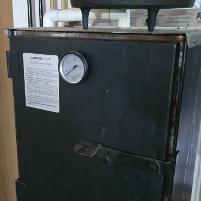 Sale Photo Thumbnail #21: Black electric smoker box with built-in temperature gauge, topped with a vintage cast iron Dutch oven with legs.