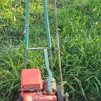Sale Photo Thumbnail #94: Vintage Power Trim gas-powered walk-behind lawn edger with a red engine, teal frame, and dual handles, showing visible wear and rust consistent with age.