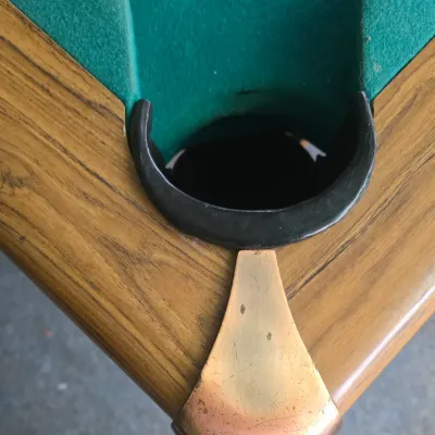 Sale Photo Thumbnail #114: Close-up view of a pool table corner pocket featuring green felt, a wooden rail, and a brass-finished corner accent.