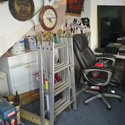 Sale Photo Thumbnail #38: Collection of workshop equipment and home bar decor, including a multi-position aluminum ladder, Ryobi drill press, black leather office chair, and vintage brewery barrel-head signs.