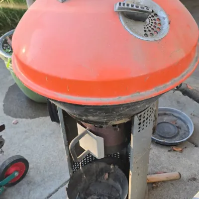 Sale Photo Thumbnail #89: Vintage orange kettle-style charcoal grill on a wheeled metal cart, showing light weathering and wear from outdoor use.