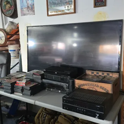 Sale Photo Thumbnail #48: Home entertainment setup featuring a large flat-screen television, Yamaha AV receiver, media players, stacked DVDs, and framed bar signs mounted on the wall.