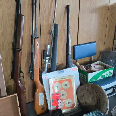 Sale Photo Thumbnail #59: Collection of vintage air rifles, paper shooting targets, comic books, a Masterpiece board game, and assorted collectibles displayed against wood paneling.
