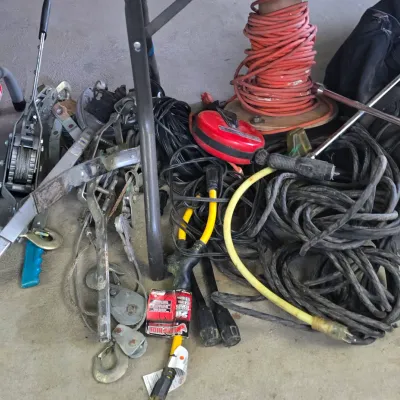 Sale Photo Thumbnail #44: Assorted heavy-duty hardware including a large spool of orange extension cord, various electrical cables, winches, and rigging pulleys stored on the floor.