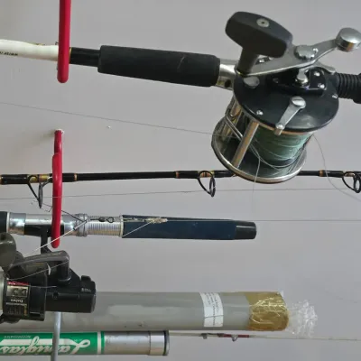 Sale Photo Thumbnail #49: Collection of fishing rods and reels, including conventional and spinning reels from brands like Daiwa, stored on a ceiling rack.