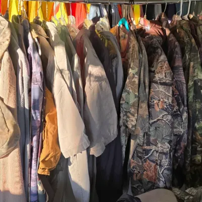 Sale Photo Thumbnail #99: Clothing rack filled with men's outdoor and hunting apparel, featuring camouflage patterns and khaki shirts.
