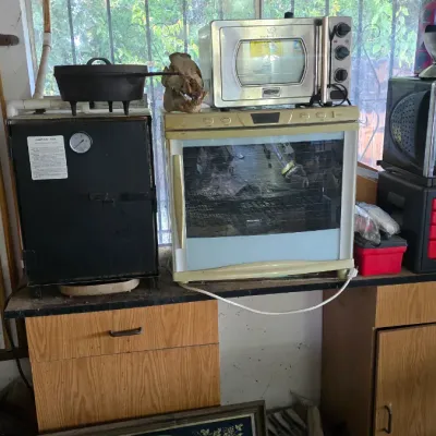 Sale Photo Thumbnail #102: Collection of kitchen appliances and breweriana, including countertop ovens, a black food smoker, cast iron cookware, and vintage framed beer signs.