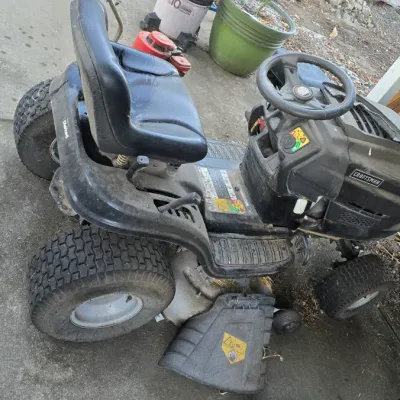 Sale Photo Thumbnail #37: Black Craftsman riding lawn mower featuring a high-back vinyl seat, side discharge deck, and steering wheel, showing light surface wear and dirt from outdoor use.
