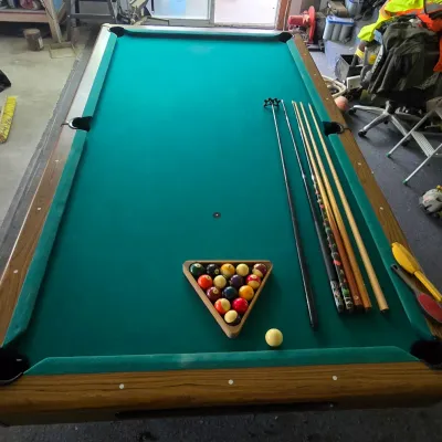Sale Photo Thumbnail #110: Full-size pool table with green felt and faux-wood trim, complete with a racked set of billiard balls, cue sticks, and bridge head.