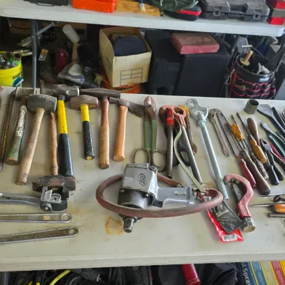 Sale Photo Thumbnail #72: Assortment of vintage hand and power tools laid out on a table, including hammers, wrenches, pliers, screwdrivers, and air-powered impact tools.