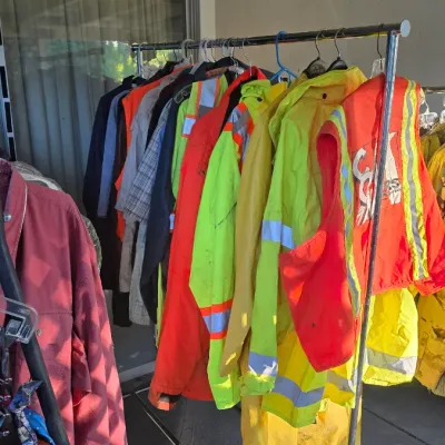 Sale Photo Thumbnail #100: Rolling metal clothing rack filled with high-visibility safety apparel, rain gear, and work jackets.